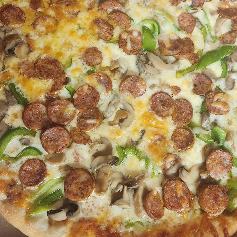 Close-up of a Bakers Corner Pizza with sausage, mushrooms, green peppers, and melted cheese.