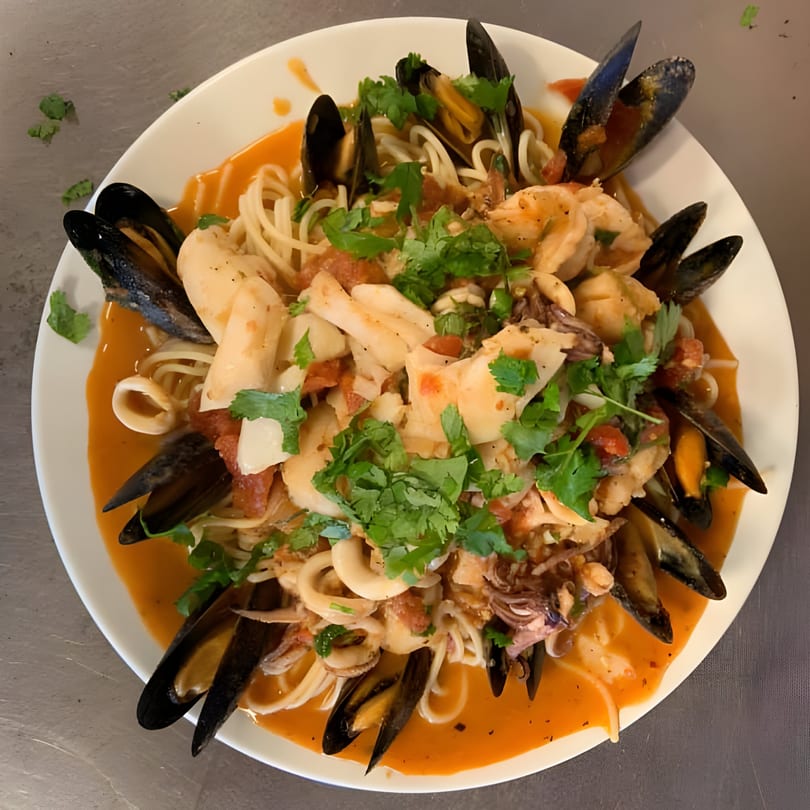 Seafood pasta with mussels, calamari, and shrimp in a red sauce, garnished with fresh cilantro.
